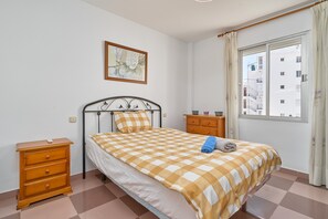 A bedroom with a bed, a nightstand, a dresser, a window with curtains, and a wall-mounted picture.
