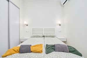 A double bed with patterned bedding, two bedside tables, wall-mounted lamps, and a white wall with an air conditioning unit. - Apartment 'Calle Antonio Millón' with Balcony, Wi-Fi and Air Conditioning (Nerja)