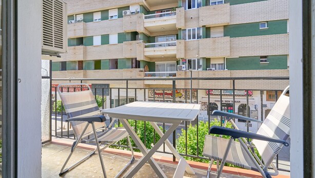 Un balcón con mesa y sillas, con vistas a un edificio de varios pisos con balcones.