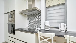 Una cocina moderna con horno empotrado, cafetera y sillas blancas.