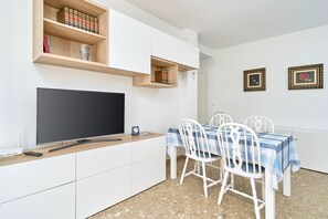 A room with a flat-screen TV, white cabinets, a dining table with chairs, and two framed pictures on the wall. - Apartment 'Calle Antonio Millón' with Balcony, Wi-Fi and Air Conditioning (Nerja)