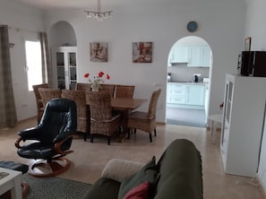 A living room with a dining area, a black leather chair, a green sofa, and a kitchen in the background.