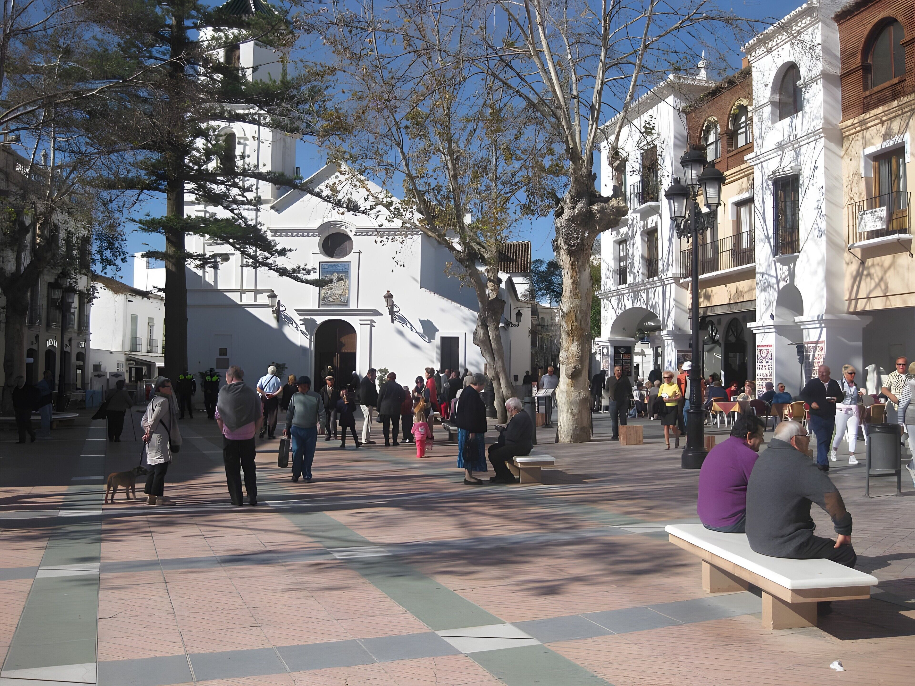A public square with people, benches, and historic buildings.