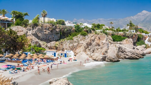 Ein Strand mit Felsen, Sonnenschirmen und Menschen.