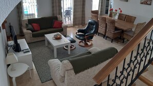 Ein Wohnzimmer mit einer Couch, einem Couchtisch, einem Fernseher, einem Essbereich mit Stühlen und einer Treppe.