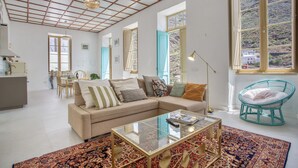 Un salon avec un canapé, une table basse et un fauteuil. On aperçoit un coin repas au fond de la pièce.