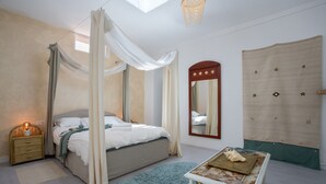 Une chambre à coucher avec un lit à baldaquin, une table de chevet, une commode et une table ornée d’un objet décoratif.