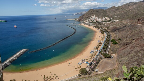 Une ville côtière dotée d’une plage, d’une jetée et bordée par une chaîne de montagnes.