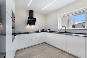 Une cuisine moderne avec des meubles blancs, une hotte noire, une fenêtre offrant une belle vue et un plancher en bois clair.