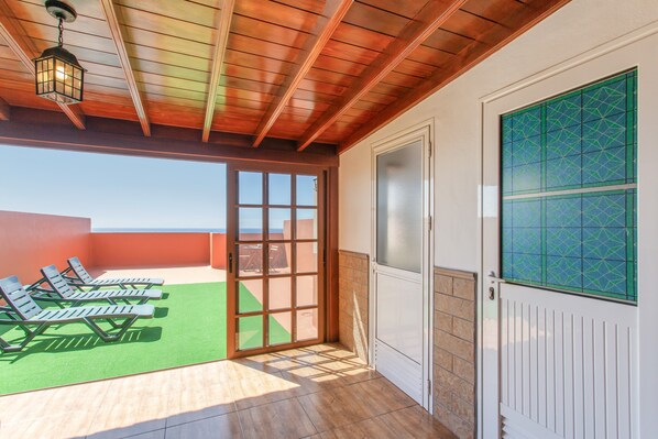 Un espace extĂ©rieur abritĂ©, dotĂ© dâun plafond en bois, dâune porte-fenĂȘtre coulissante et offrant une vue sur le ciel.
