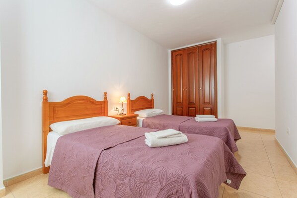 Un dormitorio con dos camas, cabeceros de madera, una mesita de noche con lámpara y un armario.