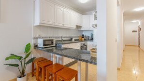 A kitchen with white cabinets, a granite countertop, a microwave, and a sink. There are wooden stools and a potted plant. - Vacation 'Candelaria 1' with Sea View, Wi-Fi and Air Conditioning (Candelaria)