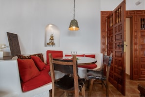 Een eetruimte met een ronde tafel, rode kussens en een hanglamp.