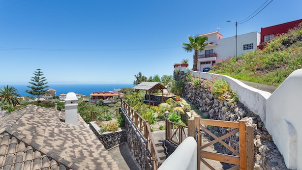 A coastal residential area with a stone staircase leading to a white building with a red roof, surrounded by greenery and a clear view of the sea. - Vacation Home 'Volcán 18' with Sea View, Private Terrace and Wi-Fi (El Tanque)