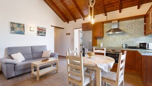 A cozy living area with a sofa, a dining table, wooden chairs, a kitchen with a stove, microwave, and patterned backsplash. - Vacation Home 'Volcán 18' with Sea View, Private Terrace and Wi-Fi (El Tanque)