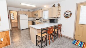 A compact kitchen with a central island, wooden bar stools, and a microwave. - Short Walk To The Beach, Water Views, Screened in Porch, Sun Deck (Salvo)
