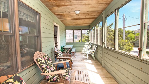 A covered porch with wooden furniture, large windows, and a view of the neighborhood. - Short Walk To The Beach, Water Views, Screened in Porch, Sun Deck (Salvo)