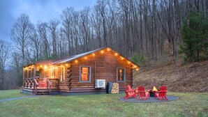 Un chalet rustique en rondins de bois, doté d’un porche, d’un foyer extérieur et de sièges pour profiter de l’extérieur.