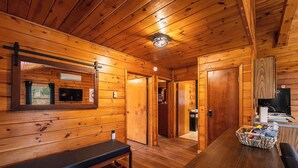 L’intérieur d’un chalet en bois, avec un banc, une table sur laquelle se trouve un panier et une cheminée.