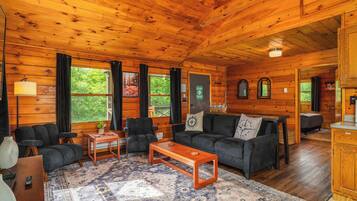 L’intérieur d’un chalet en bois, avec un canapé, des fauteuils, une table basse et un tapis.