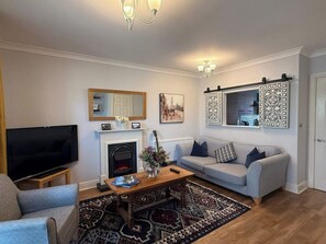Cozy living area with a sofa, armchair, flat-screen TV, fireplace, and decorative mirror.