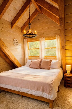Une chambre confortable avec un plafond en bois, un lit avec une literie blanche, deux oreillers, un luminaire suspendu et une fenêtre avec des rideaux.