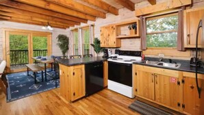 A rustic cabin kitchen with wooden cabinets, a black stove, and a large window.