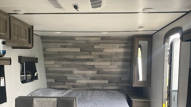 Interior compacto de uma RV com cama, área de jantar e espaço para sentar.