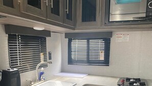 Cozinha compacta com micro-ondas embutido, pia e fogão. Armários de madeira e janela com persianas.
