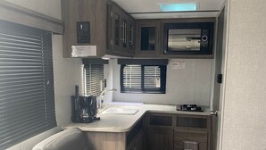 Interior de uma caravana compacta, com cozinha compacta, área de estar acolchoada e uma pequena janela.