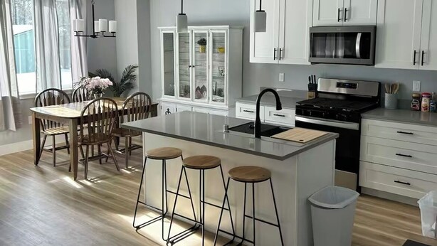 A modern kitchen with white cabinets, a central island with stools, a microwave, and a stove.