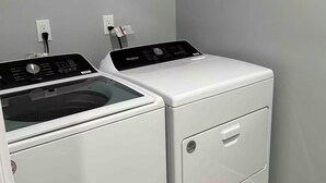 A laundry room with two stacked washers and dryers, a power outlet, and a wooden floor.