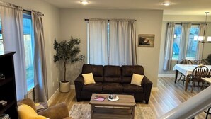 A living room with a brown leather sofa, a coffee table, and a dining area with a table and chairs.
