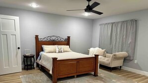 A bedroom with a wooden bed, a bedside table, a chair, a ceiling fan, and a window with curtains.