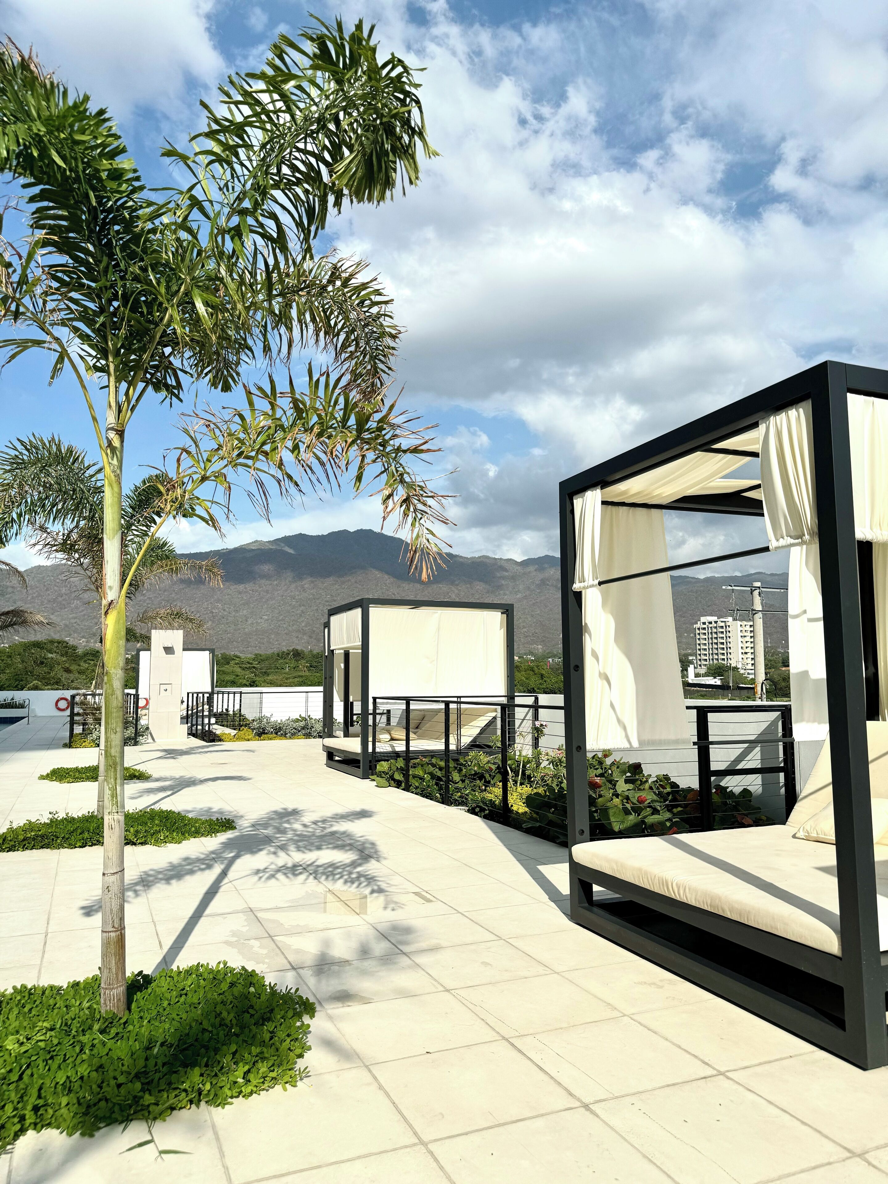 A modern outdoor seating area with a canopy bed, surrounded by greenery and a view of distant mountains.