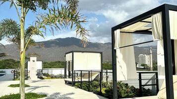 A modern outdoor seating area with a canopy bed, surrounded by greenery and a view of distant mountains.