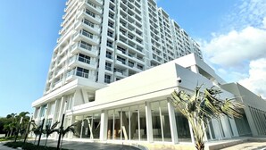 A modern multi-story hotel with a prominent entrance, a covered area with palm trees, and a clear sky. - Nature and Ocean View Suite With Hot Tub steps to beach in Santa Marta (Santa Marta)