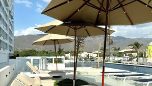 A poolside area with lounge chairs and umbrellas, a pool, and a mountain backdrop. - Nature and Ocean View Suite With Hot Tub steps to beach in Santa Marta (Santa Marta)