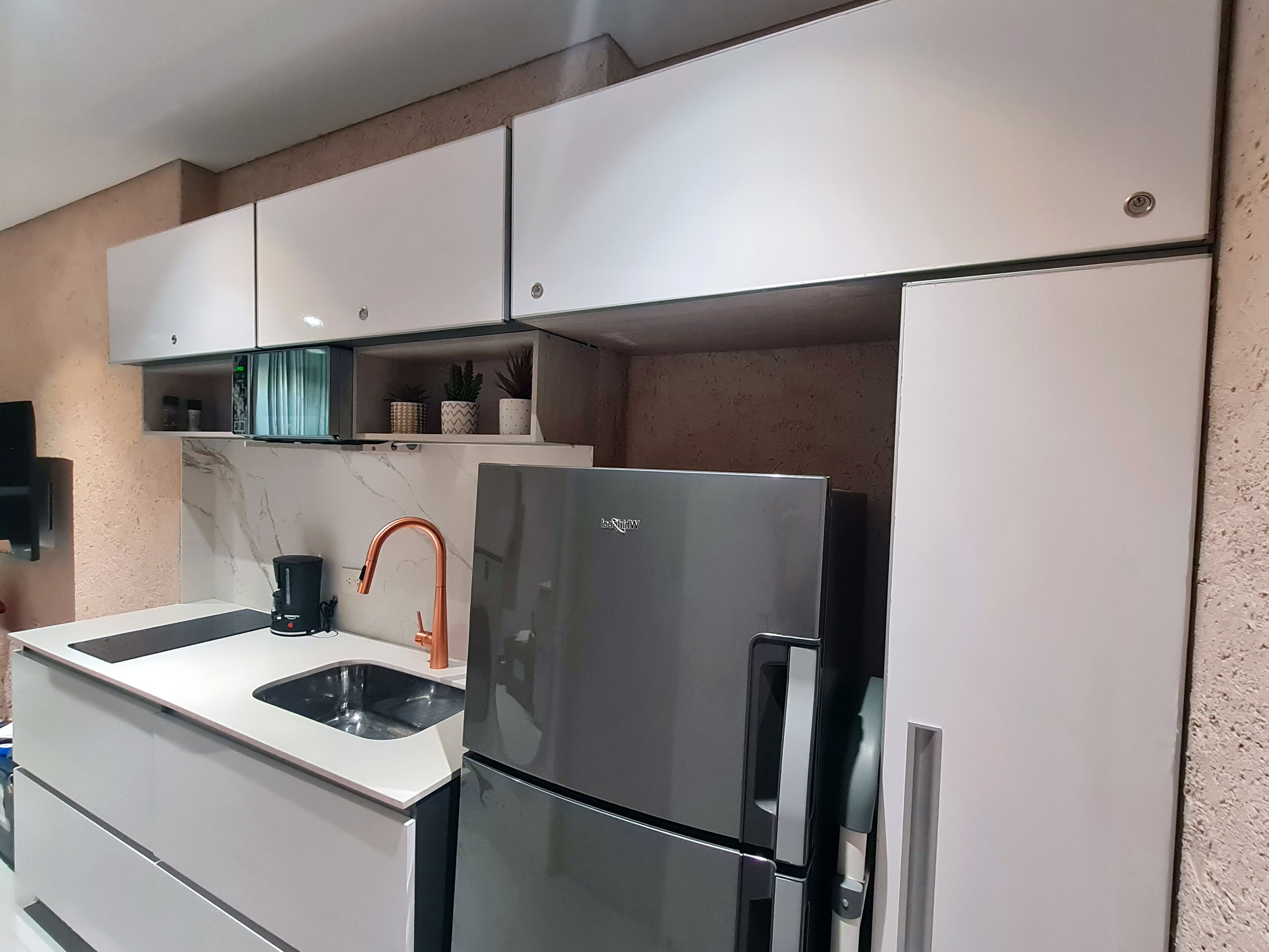 A modern kitchen with white cabinetry, a stainless steel refrigerator, a sink, and a coffee maker.