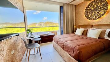 Un dormitorio con una cama grande, una mesa de comedor y una silla, un ventilador de techo y vistas al paisaje.