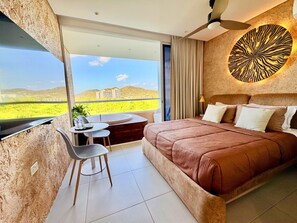 A bedroom with a large bed, a dining table, and a chair, a ceiling fan, and a view of the landscape. - Nature and Ocean View Suite With Hot Tub steps to beach in Santa Marta (Santa Marta)