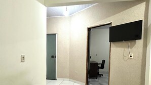 Una habitación con un sofá marrón, piso de baldosas, un televisor de pantalla plana montado en la pared y una puerta que da a otra estancia.
