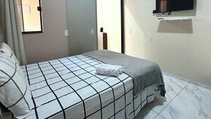 Un dormitorio con cama, aire acondicionado, televisor, puerta corredera y ventana con cortinas.