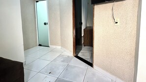 Un pasillo con piso de baldosas, una puerta, un televisor montado en la pared y una lámpara en el techo.