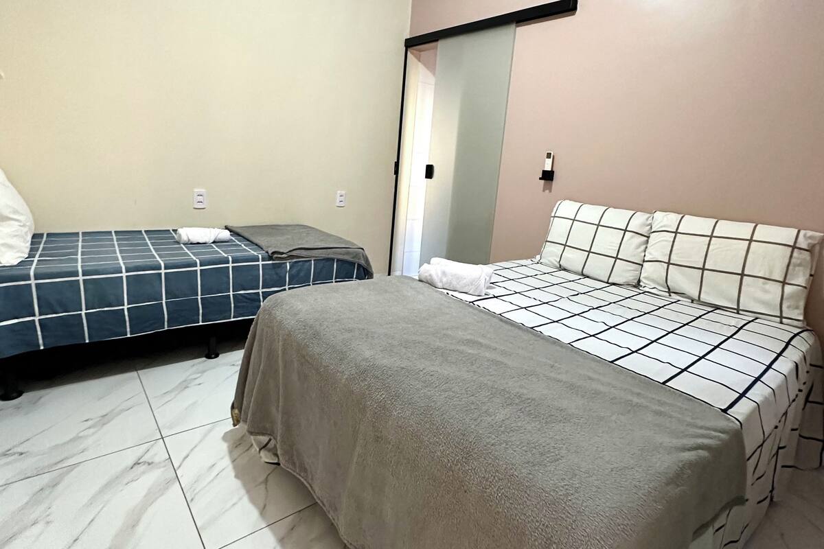 Een slaapkamer met twee bedden, waarvan er één een geruit beddegoed heeft en de ander een effen.