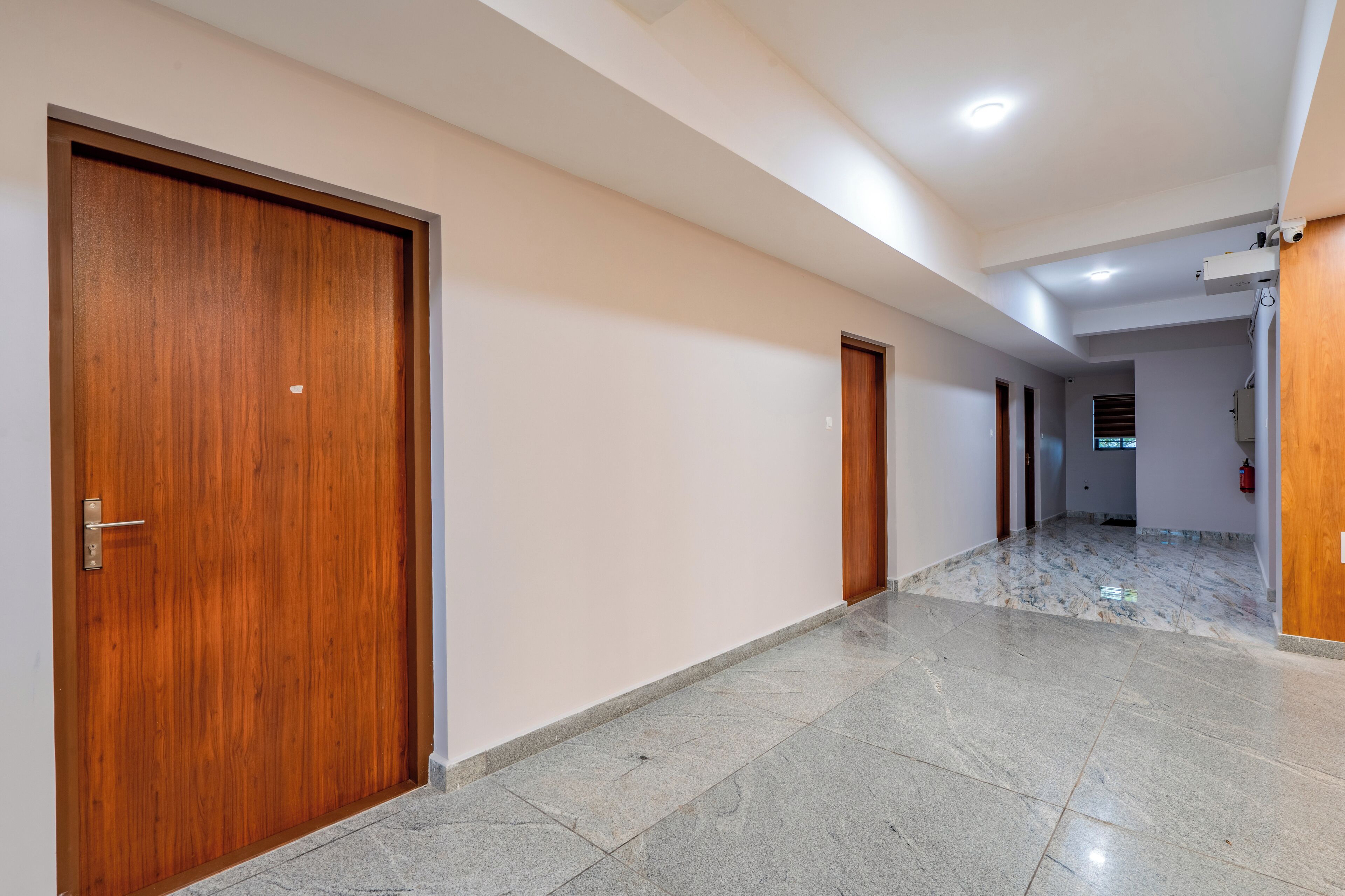 A hallway with wooden doors, a marble floor, and a ceiling with recessed lighting.