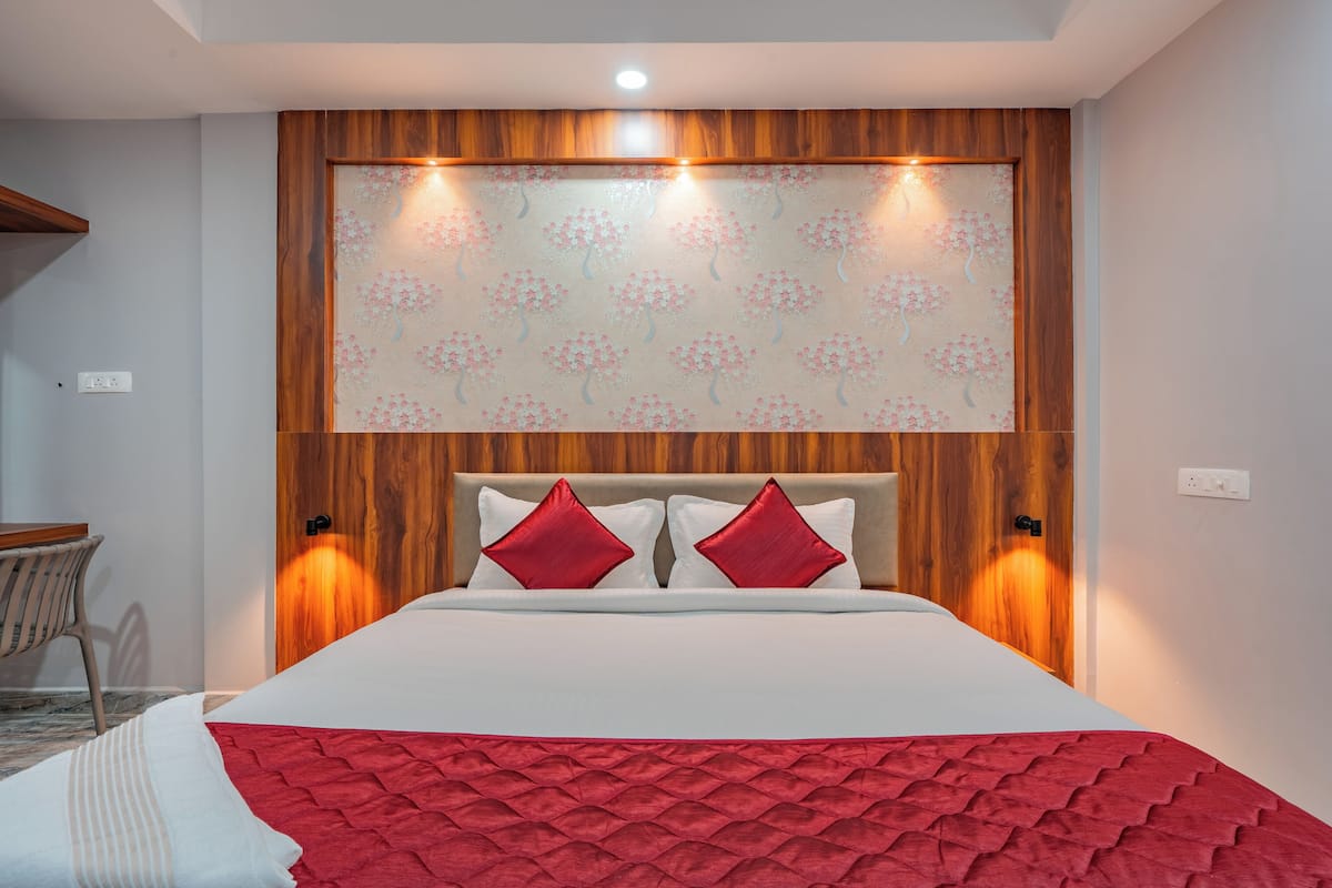 A hotel room with a wooden headboard, a large bed with red and white bedding, and two wall-mounted lights.