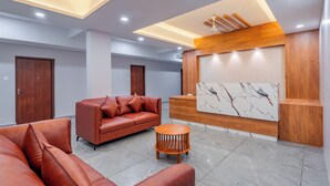 Un espace d’accueil moderne, avec un comptoir de réception en bois, un mur en marbre et un canapé en cuir.