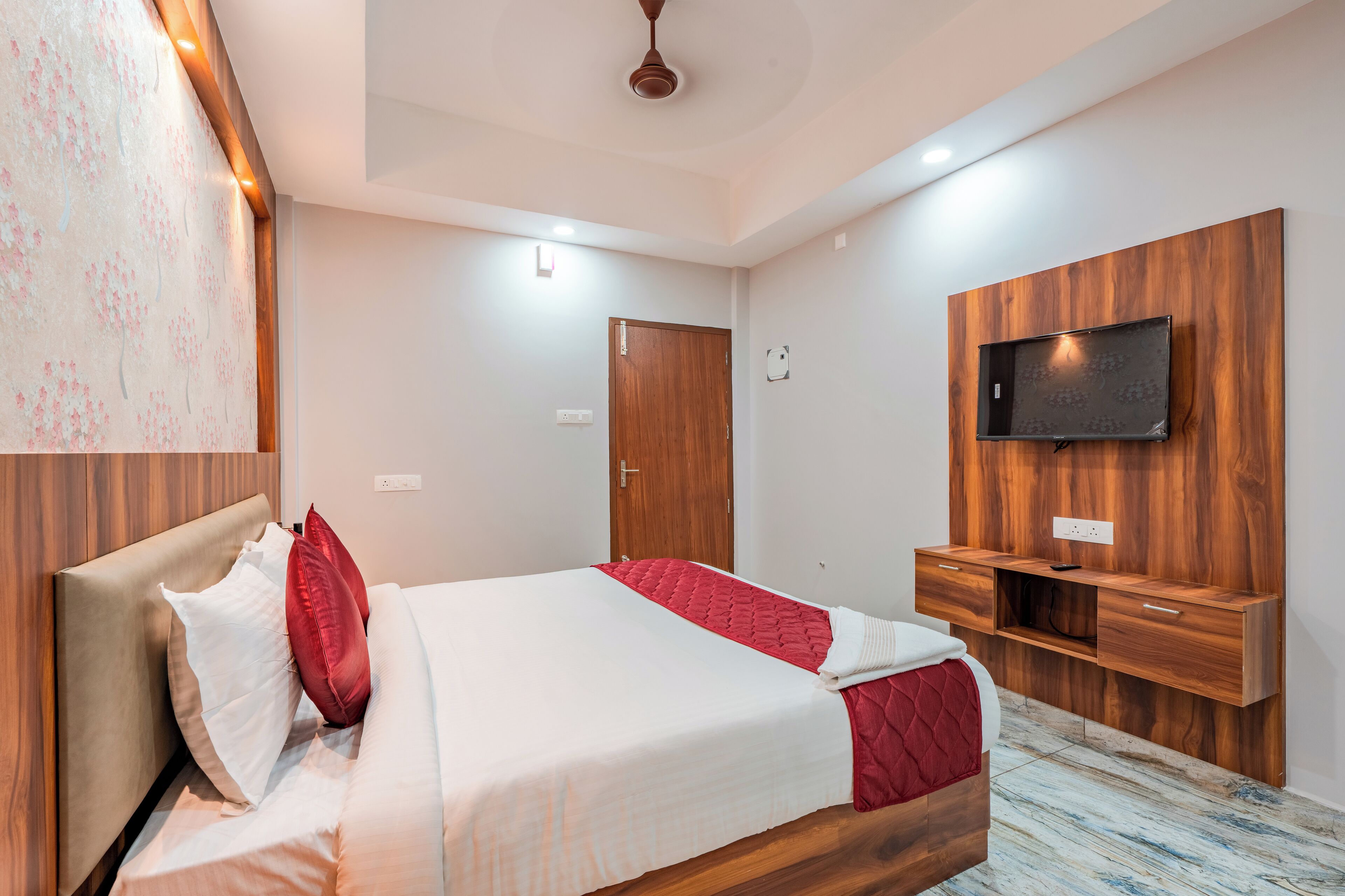 A modern hotel room with a bed, a wooden headboard, a TV mounted on the wall, and a wooden cabinet.