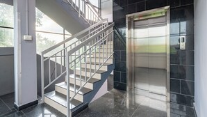 Un intérieur moderne avec un escalier et un ascenseur, de grandes fenêtres et un sol carrelé.